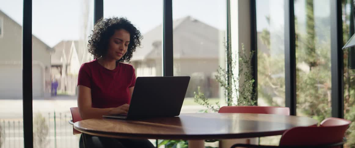 A teenager sits at a table and works on her laptop