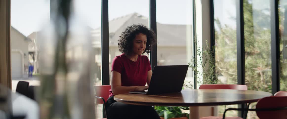 A black woman sits down at a table and starts using her laptop