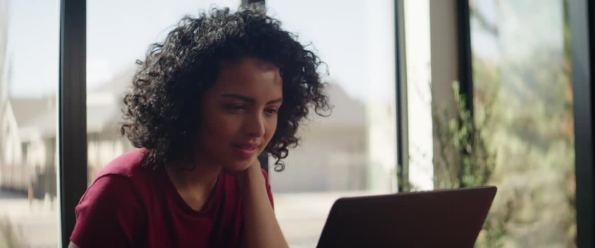 A young black woman sits indoors and uses a laptop