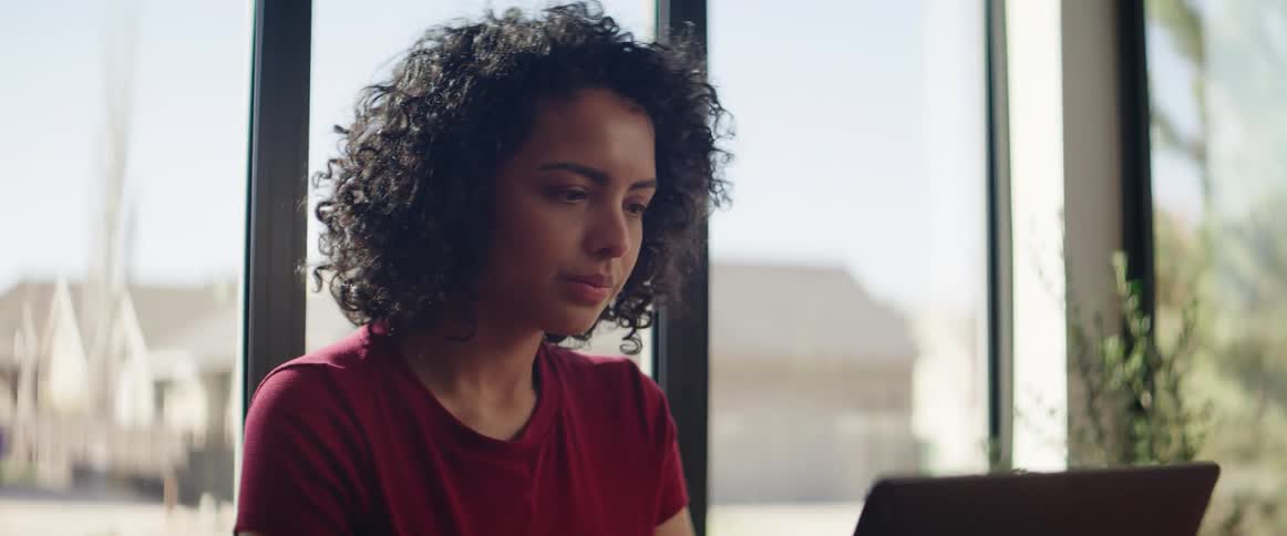 A young black woman walks over to a table sits down and gets involved in her laptop