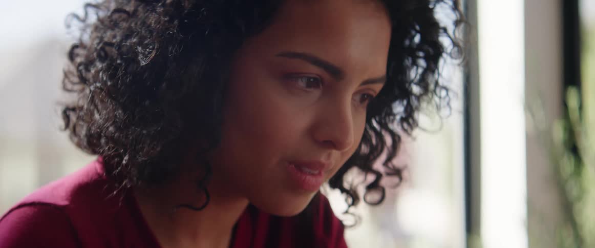 Woman with black curly hair scratches her neck then blinks her eyes