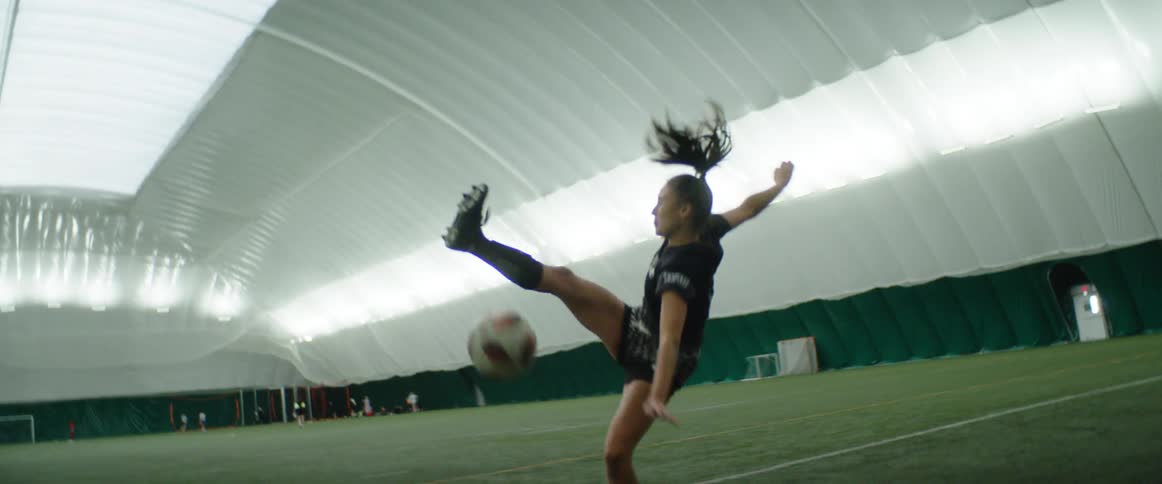 A young girls kicks at a soccer ball and falls down