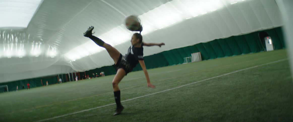 A soccer player kicks the ball into the goal in an indoor field