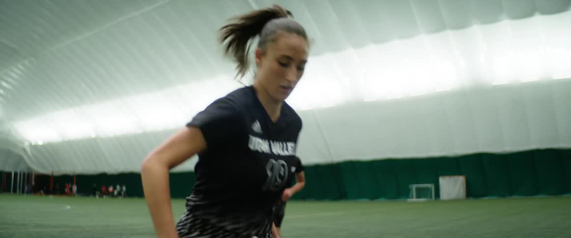 A female athlete runs down an indoor field while two other women watch