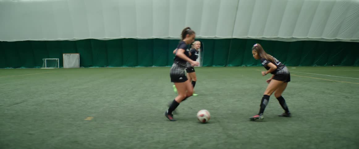 Three female soccer players scrimmage on indoor field