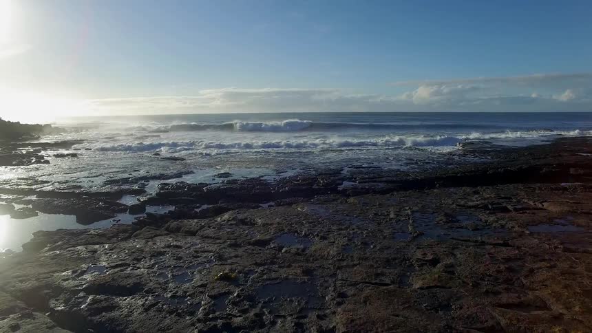 Aerial view of a field leading up to a rocky shore as the sun rises