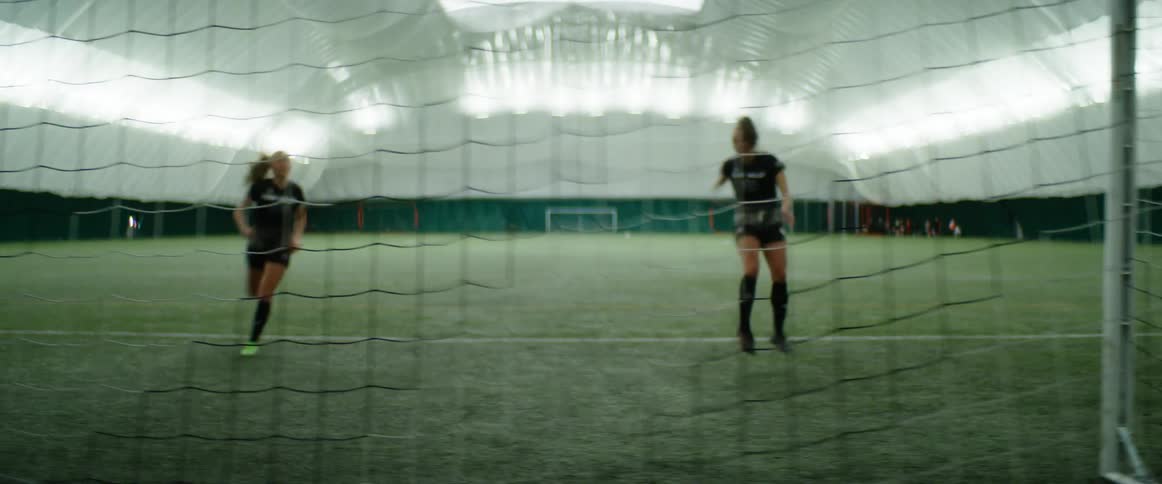 Two teenage soccer players practice kicking a ball into the goal