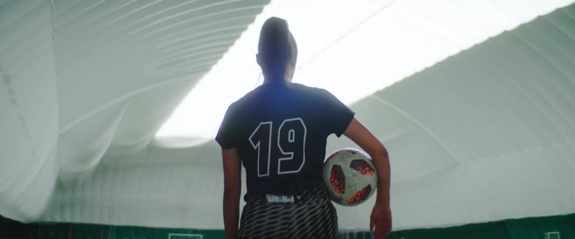A female soccer players stands in an indoor soccer field