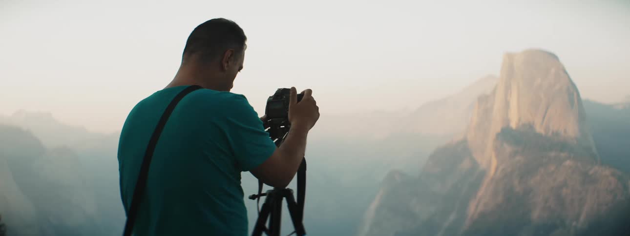 A man photographs some mountains partially covered in mist