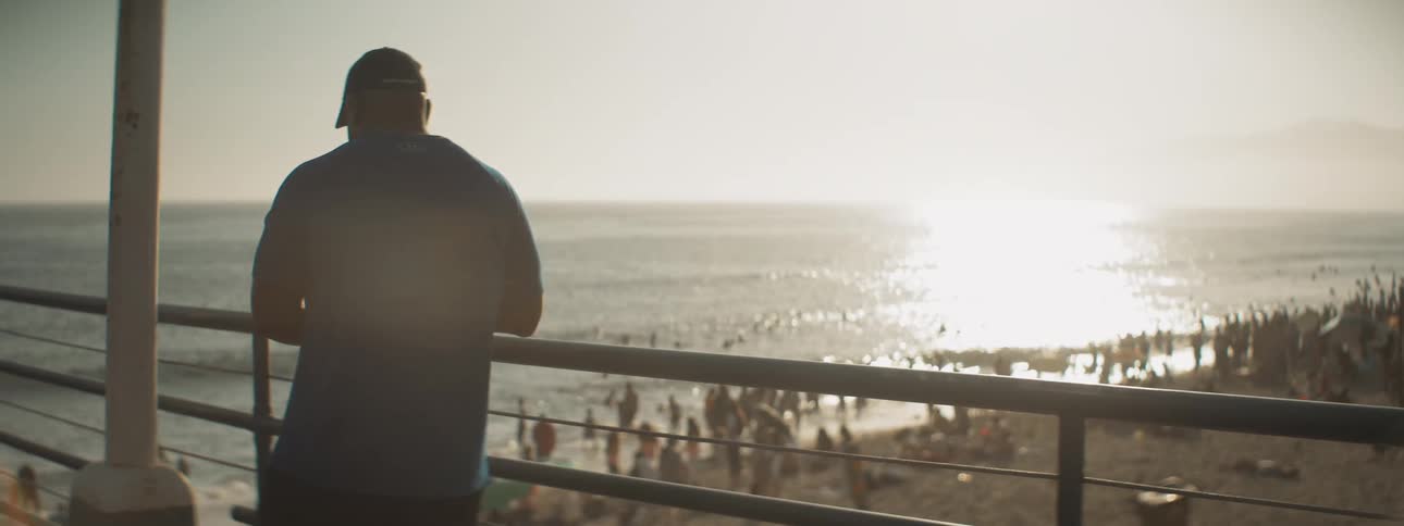 Man stands at railing on pier overlooking crowded beach