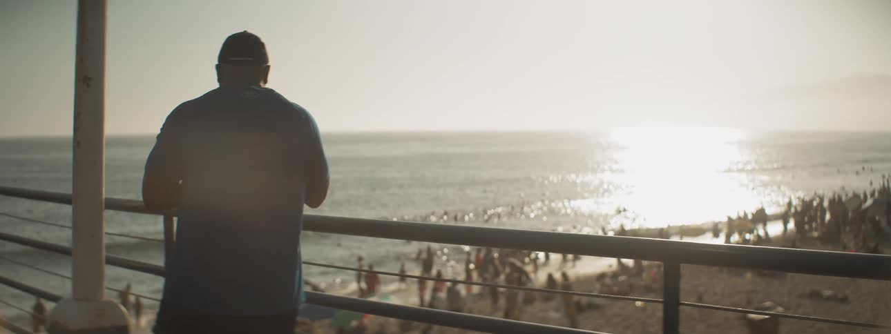 Man stands on pier overlooking crowd of tourists on beach