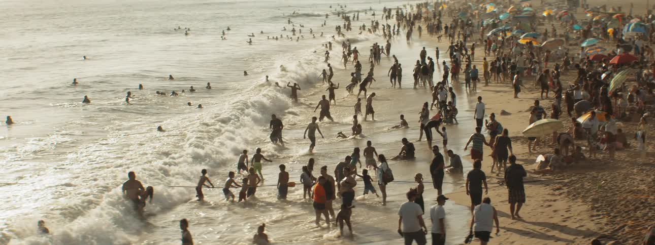 Large crowd of people at the shoreline enjoying waves at the beach