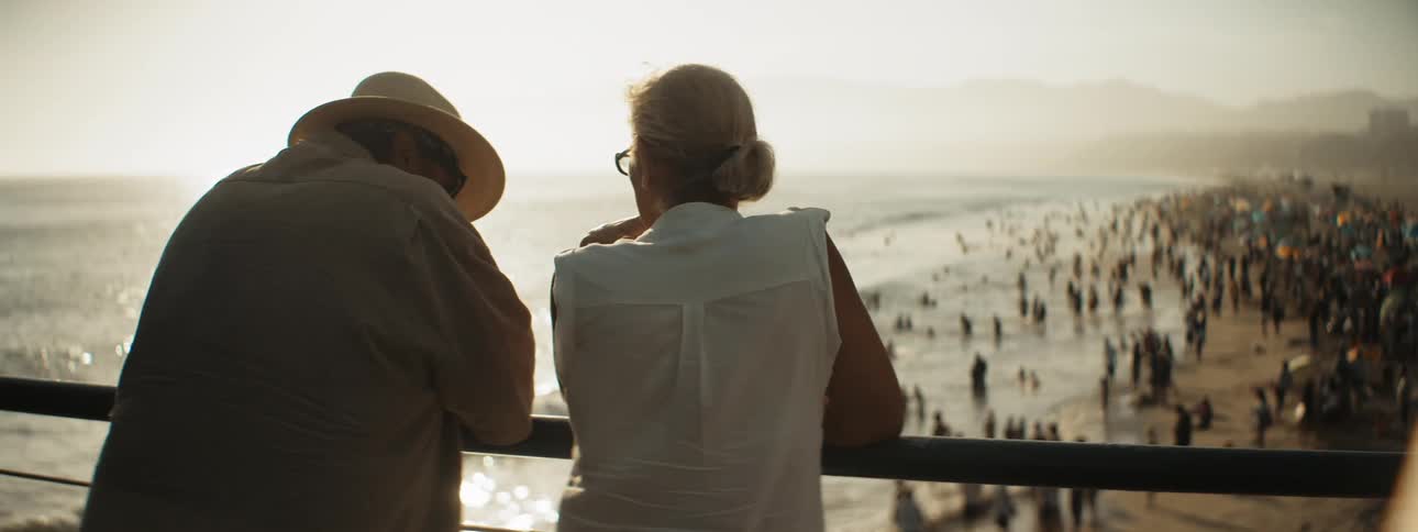 A man and woman stand on a balcony together overlooking the beach and ocean