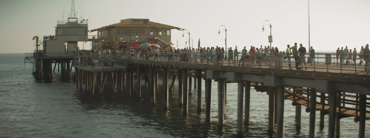 Several people are standing on a pier that juts out into the ocean