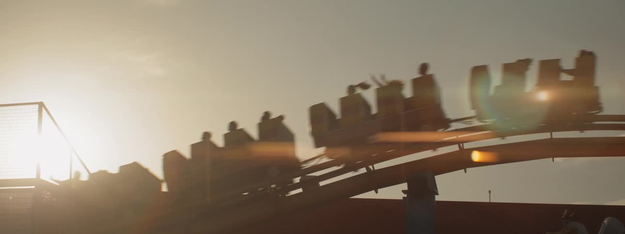 People riding roller coaster silhouetted against sky