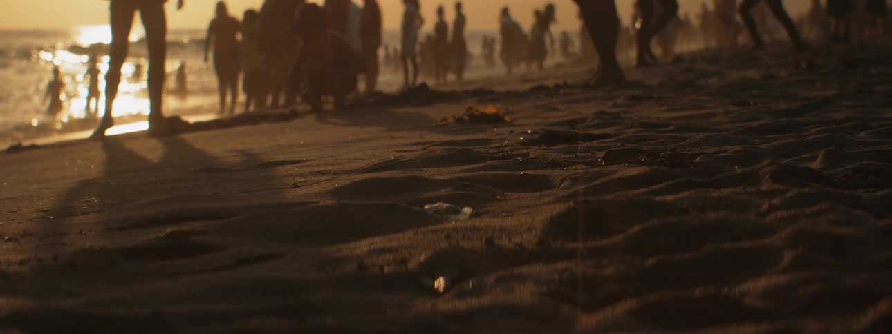 Crowd of people mingle on the beach at sunset while others swim in the lake