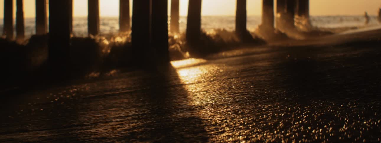 Sea waves crashing under a pier in the golden light of sunset