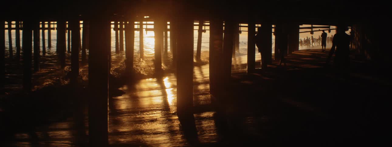 A woman walking in the darkness under a pier on a beach at sunset