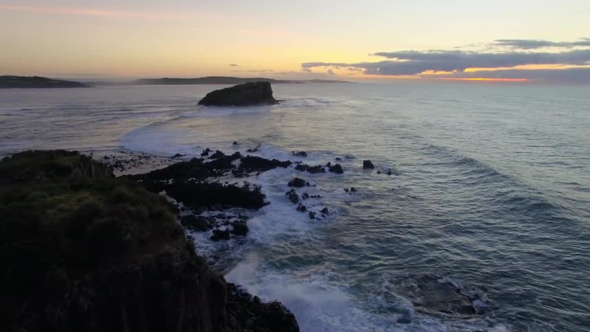 Aerial of the dawn at a rocky coast with waves and an island