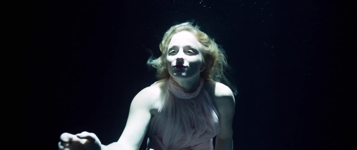 A woman floating underwater making a beckoning gesture while being illuminated from sunlight from the surface