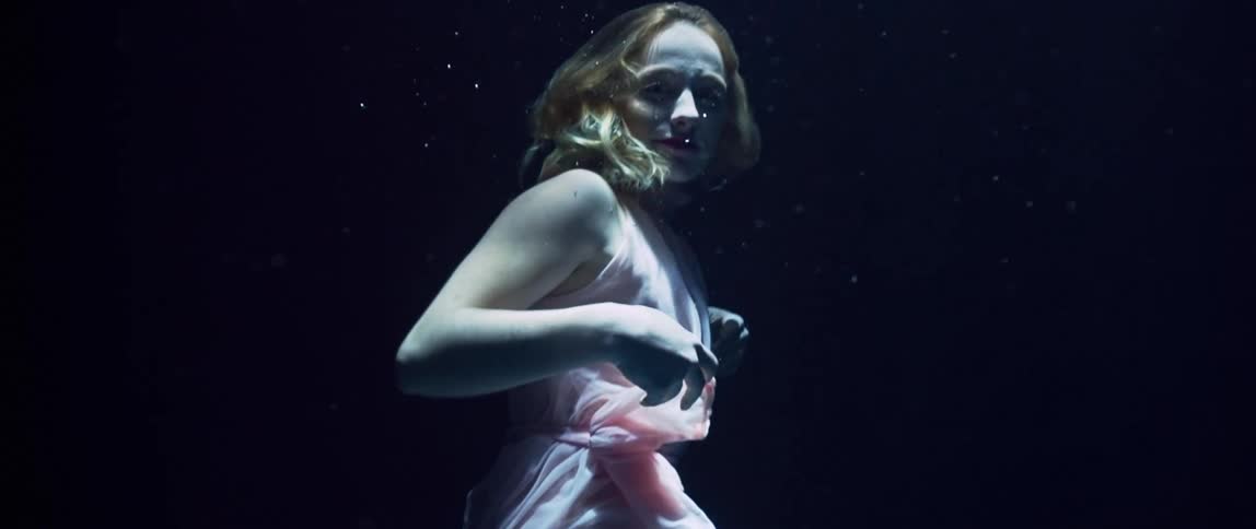 A white blonde woman in a dress swims and gestures underwater