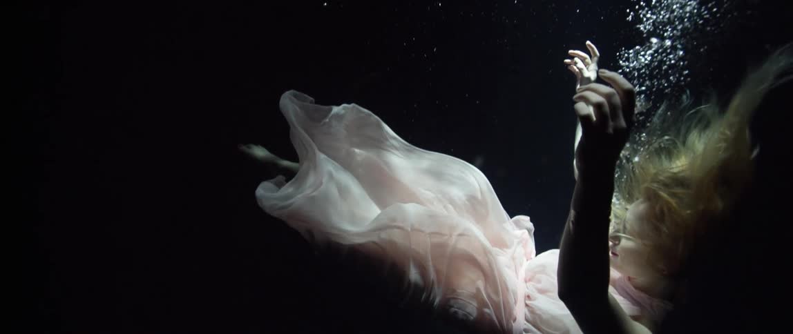 A white woman in a dress sinks to the bottom of a body of water