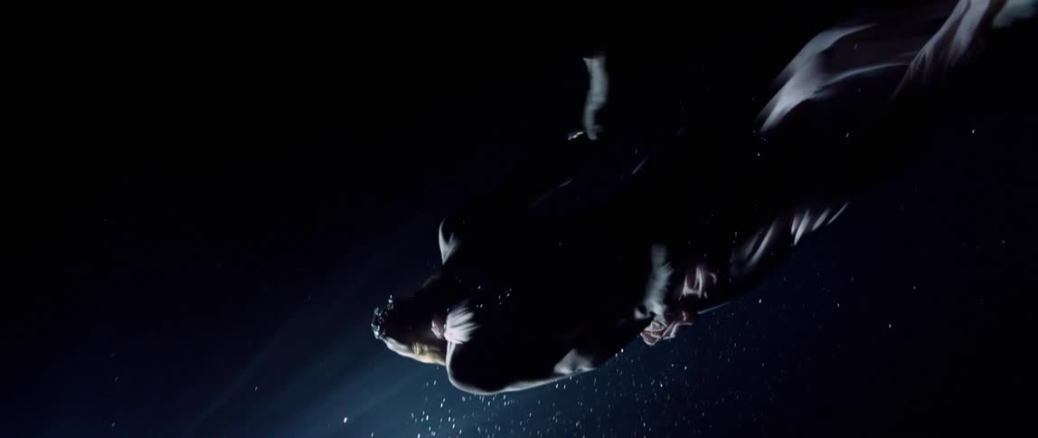 A woman in a sheer gown undulates and swims up toward a light at the surface