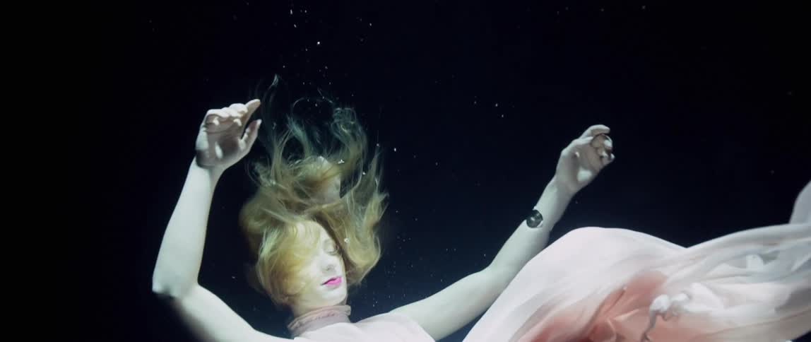 Model in long pink evening gown floats underwater with eyes closed