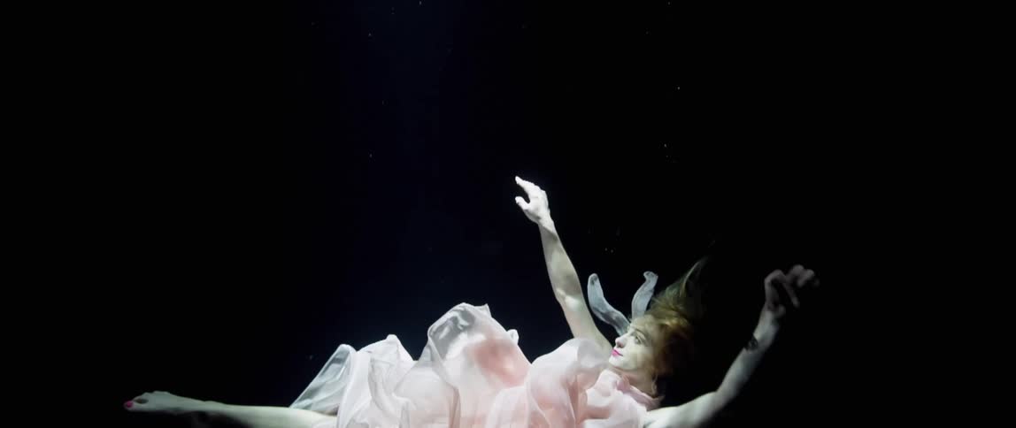 Model in gown poses and floats underwater then swims upward