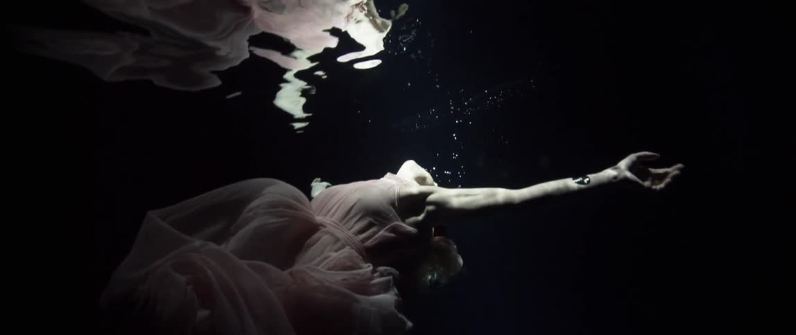 A white woman in a dress swims underwater and then surfaces