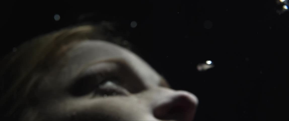 Woman floats underwater looking up toward the surface light