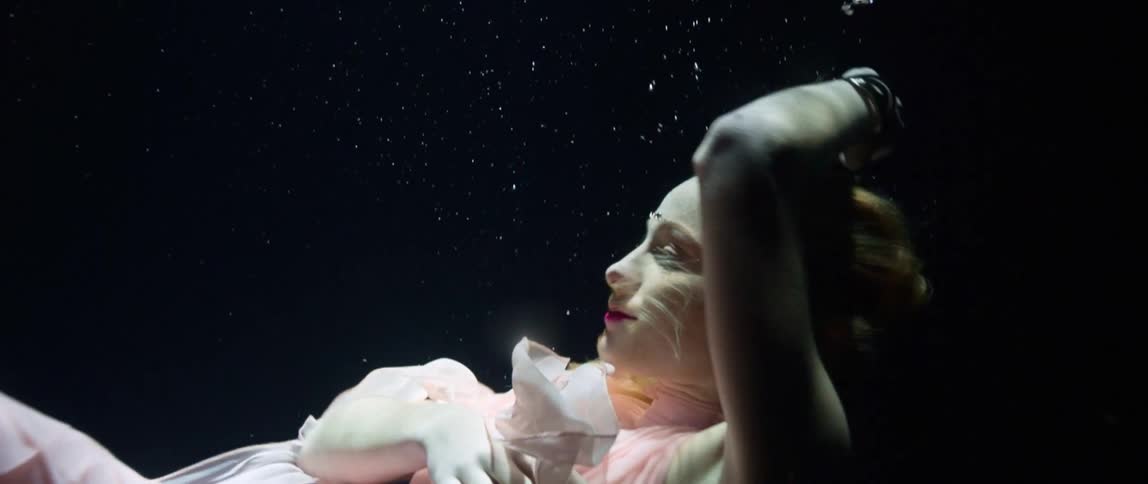 A woman in a pink dress floats and swims underwater