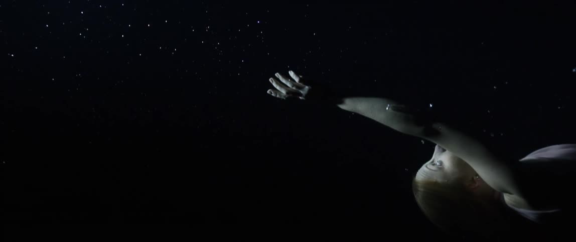 A white woman points with her hand while floating underwater
