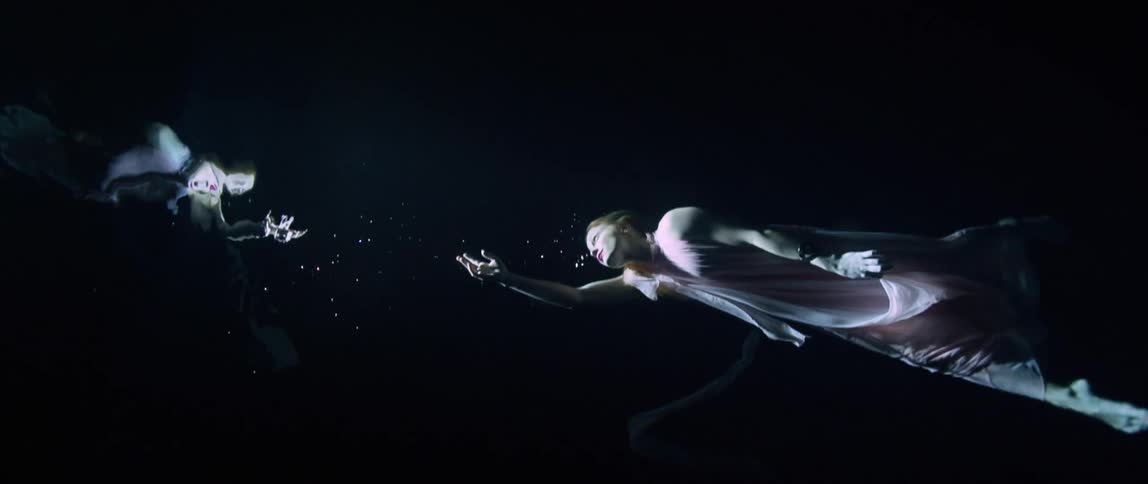 Model in pink gown underwater swims to surface with arm outstretched
