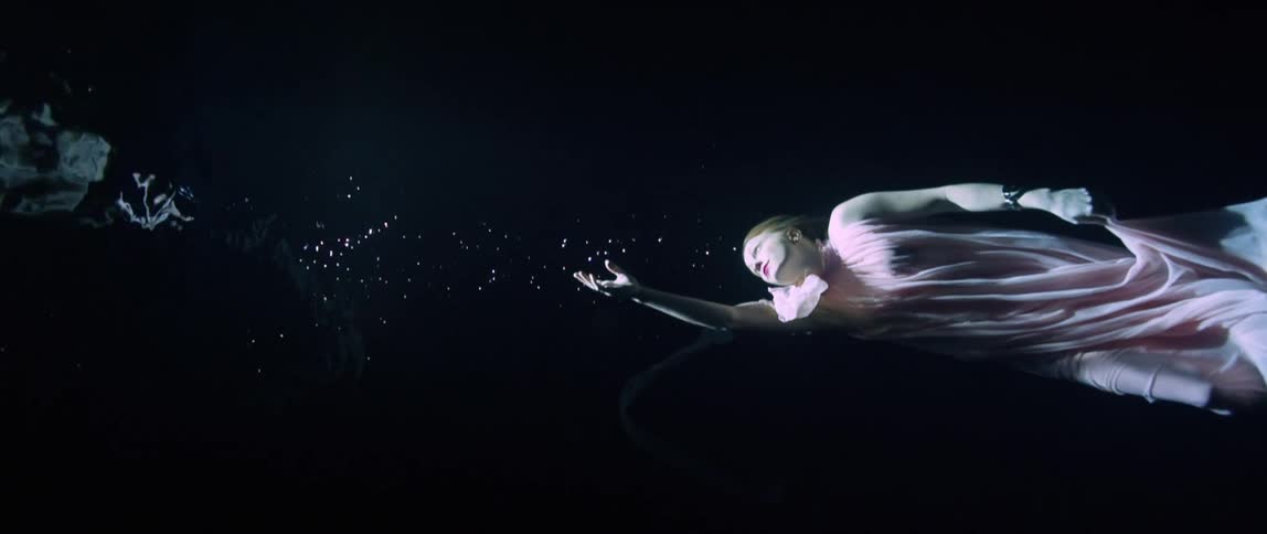 A woman underwater reaching for the surface as she is illuminated by sunlight from above