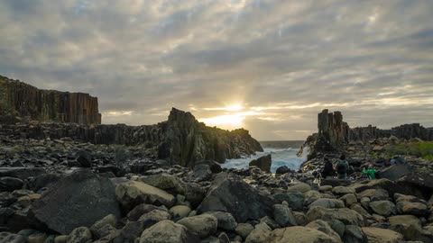 Waves crash through a rocky shoreline as photographers observe