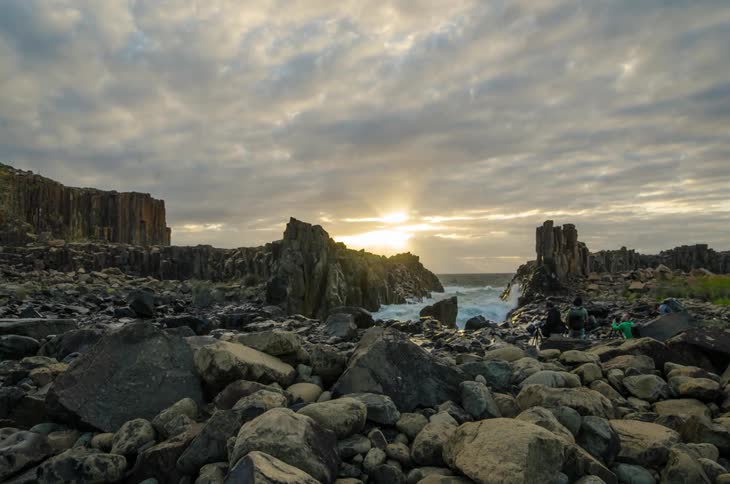 Waves crash through a rocky shoreline as photographers observe