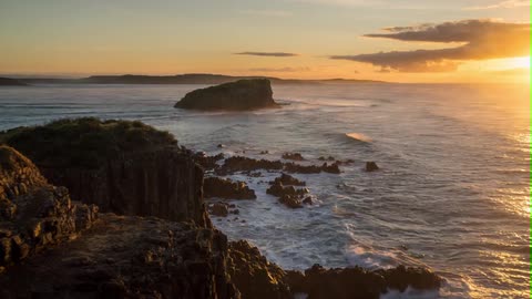Time-lapse of waves crashing against rocky coastline s as clouds drift past the rising sun