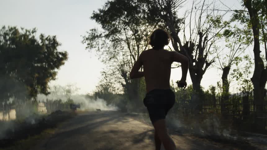 Shirtless man with short pants jogs on a dirt road in the late afternoon