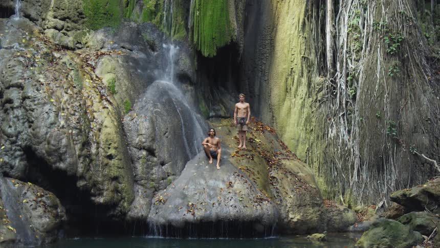 Two guys relaxing on a large rock by a waterfall in a canyon