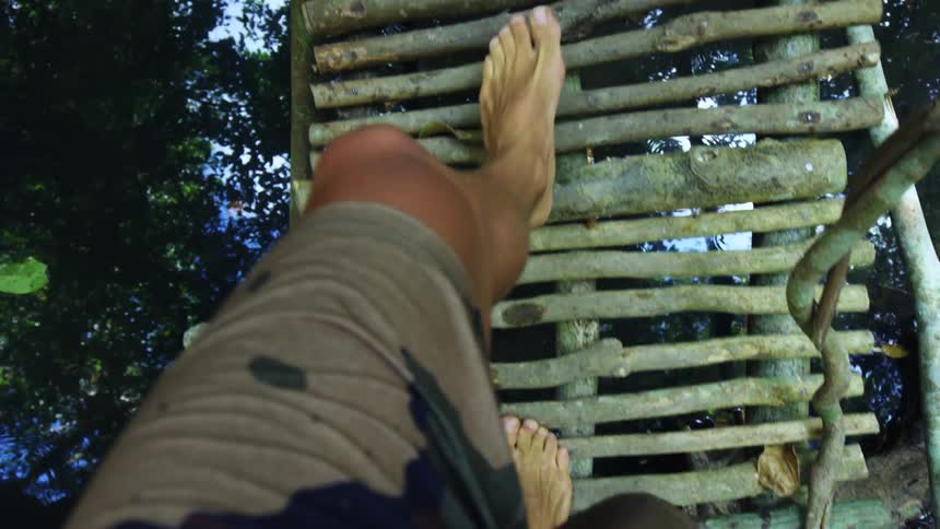 A white man walks over a narrow bridge barefoot