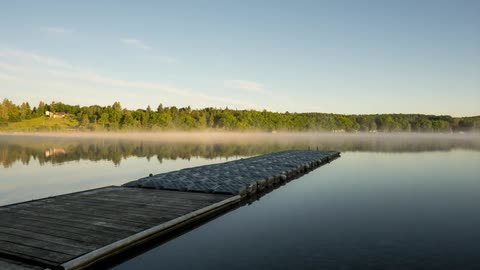 Fog rises and moves across a lake near a pier