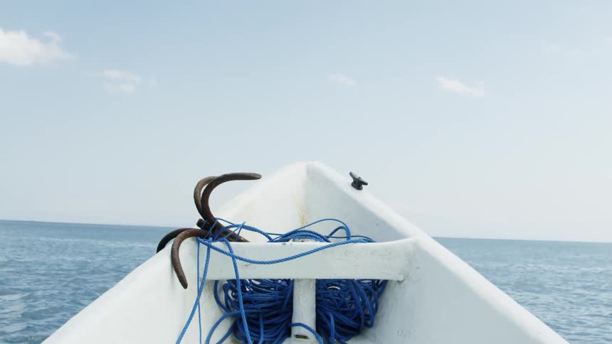 A boat containing an anchor and rope bobs on the ocean surface