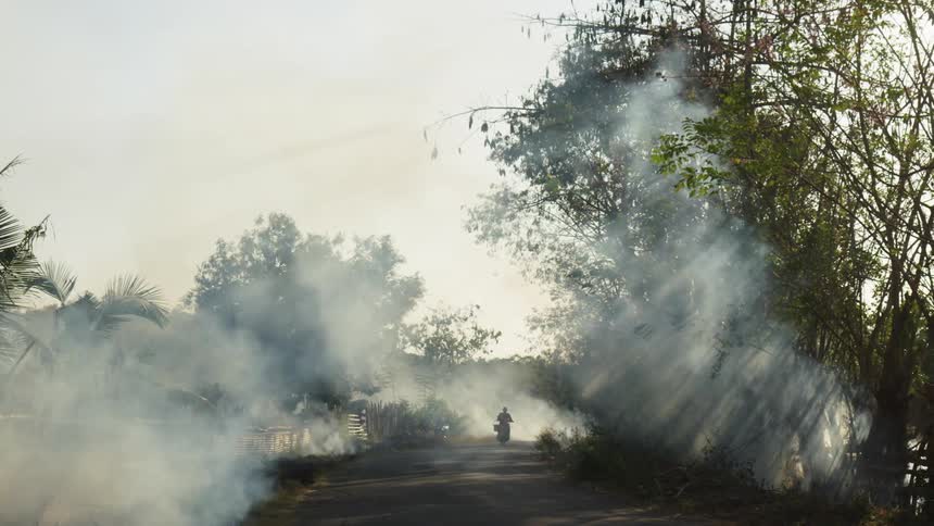 A person drives a motorcycle down a road with smoke all over it