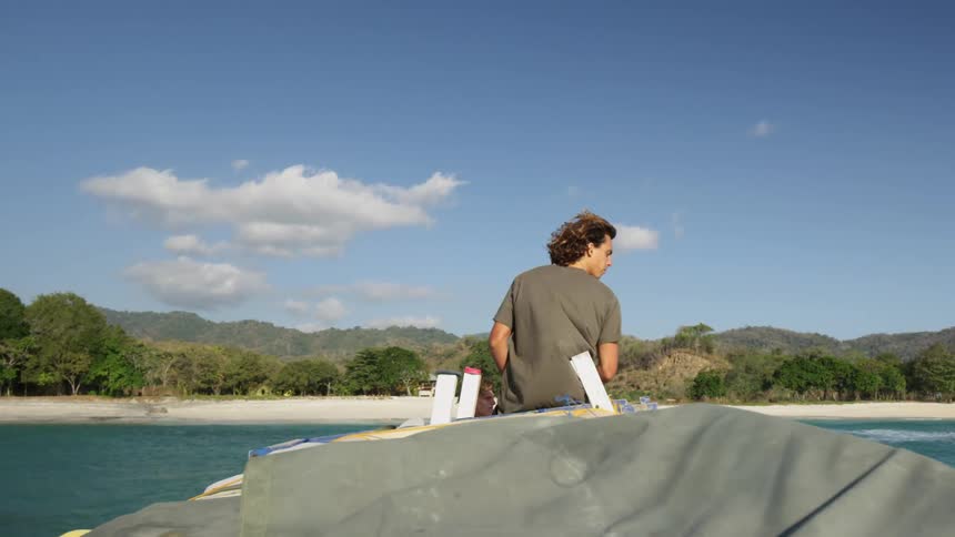 A young man sits on the end of a boat as it drives through the water