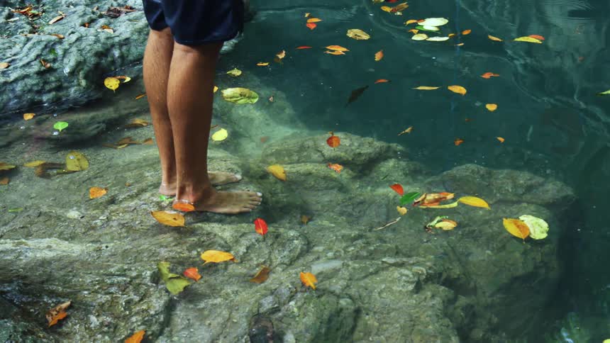 Man stands barefoot on a rock in the shore of a lake
