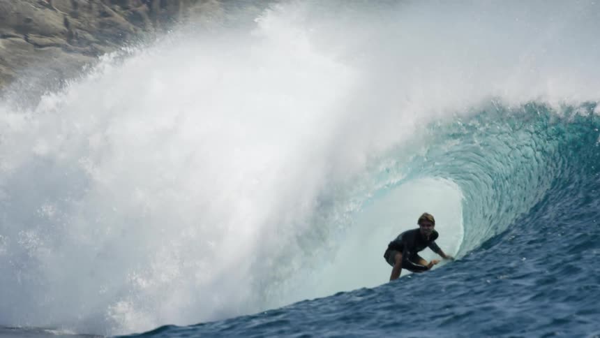 A young white man surfs a large wave off of a coast