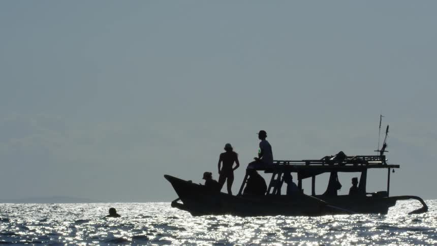 A man swims in the ocean near a boat filled with people