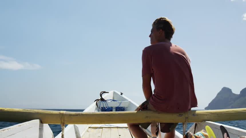 Man with red t shirt sitting on a boat looks around in the blue sea