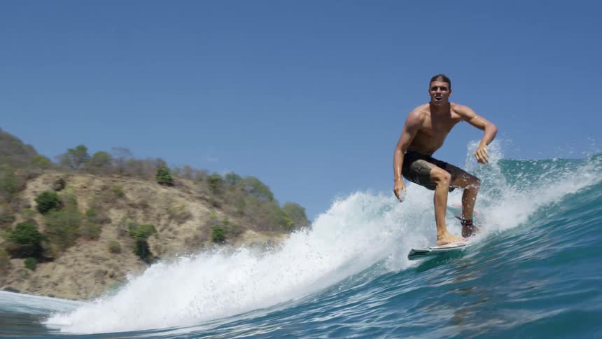 Male surfer with swimming trunks rides a wave on a surfboard